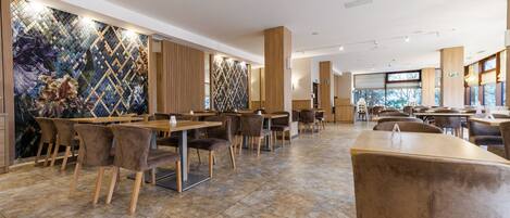 Un restaurante espacioso con techos altos, iluminación moderna y una mezcla de mobiliario de madera y tapizado.