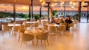 A restaurant with round tables and chairs, large windows with a view of the sea, and hanging spherical light fixtures. - Olymp IV Spa & Wellness (Kolobrzeg)
