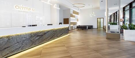 A modern reception area with a marble counter, wooden flooring, and a large mirror.