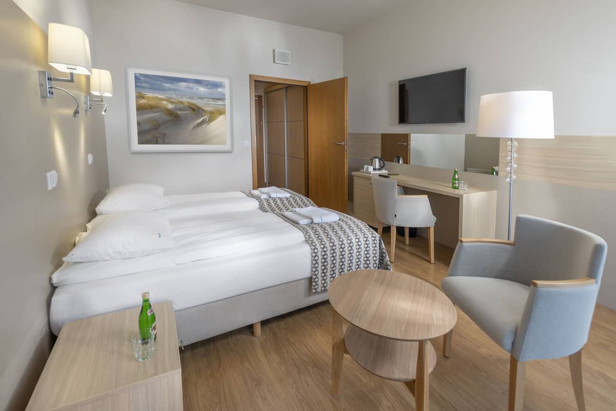 A hotel room with a bed, a desk, a chair, a TV, and a painting on the wall.