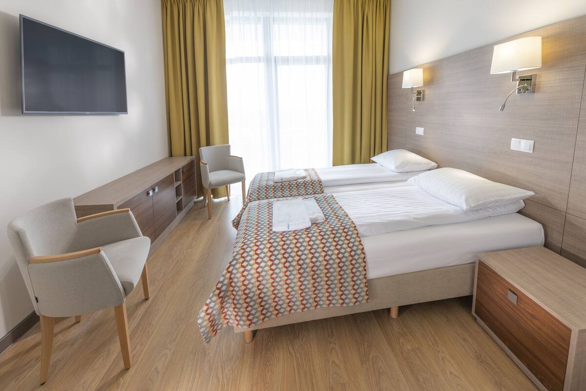 A hotel room with two beds, a TV, a desk, and a chair.