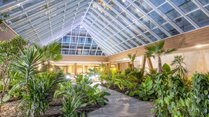 A modern atrium with a glass ceiling, surrounded by lush indoor plants and a central walkway. - Olymp IV Spa & Wellness (Kolobrzeg)