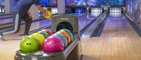 A bowling alley with a man bowling, colorful pins, and a Brunswick machine.