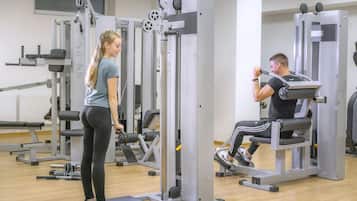 Une salle de sport équipée de matériel d’exercice, une personne debout et une autre personne utilisant un appareil.