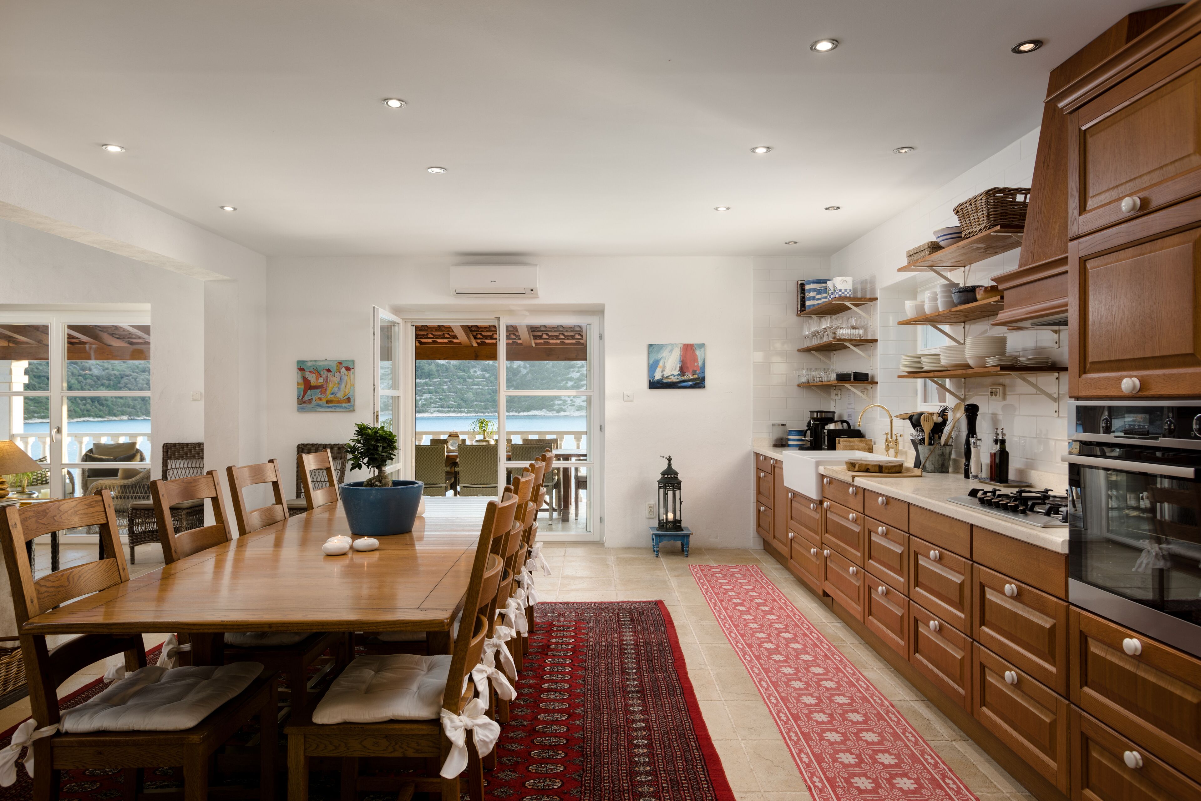 Una cocina amplia con armarios de madera, un comedor con una mesa grande y sillas, y vistas al exterior a través de un ventanal.