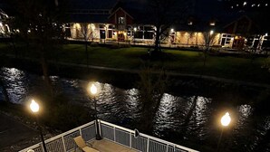 Una piscina con borde curvo, rodeada por una barandilla blanca y vista a un edificio iluminado al fondo.