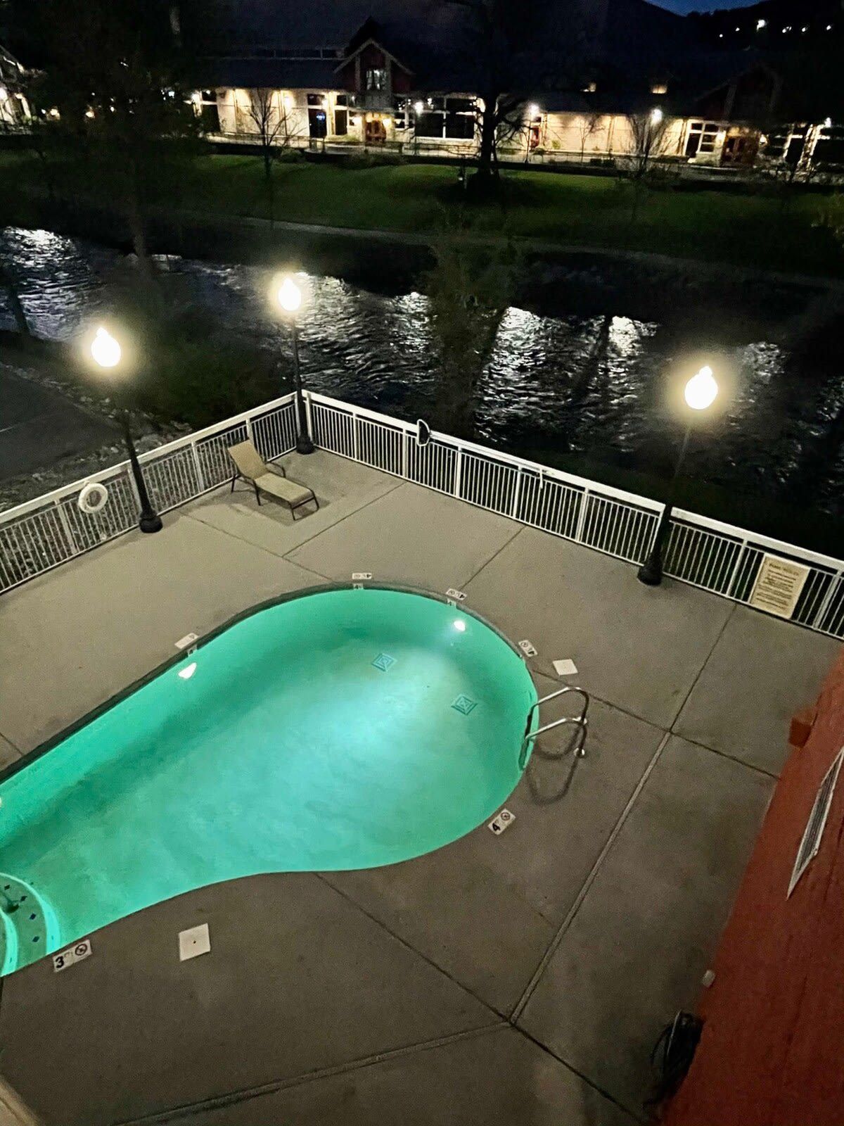 Una piscina de borde curvo, rodeada por una barandilla blanca, y una vista de un edificio al fondo.