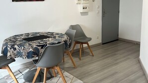Ett modernt rum med ett runt bord, två grå stolar, en blommig duk, en grå dörr och en målning som föreställer en stadsbild.