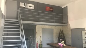 En rymlig loftvåning med en trappa som leder upp till en entresol. Ett träbord med en vas med blommor står i mitten.