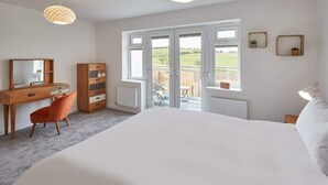 A bedroom with a large bed, a wooden desk, a chair, a dresser, and a large window with a view of the outdoors.