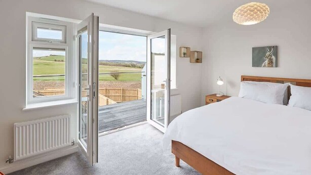 A bedroom with a large bed, a nightstand, a lamp, and a view of a green landscape through an open door.