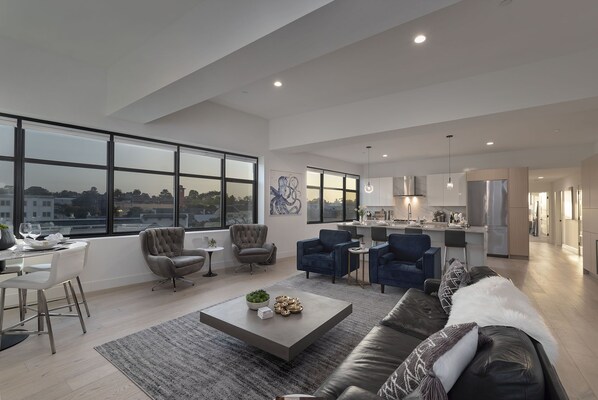 Amplia sala de estar con cocina moderna, ventanas grandes y un rincón de descanso acogedor.