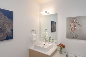 Une salle de bain moderne avec un grand miroir, un lavabo blanc et un tableau représentant un hippocampe au mur.
