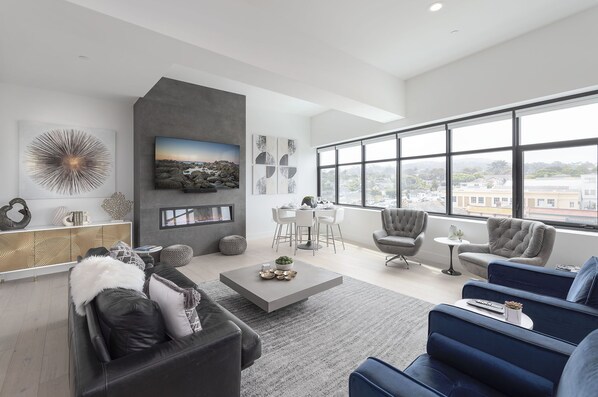 Un salon moderne avec un canapé gris, un canapé bleu, une table basse et un coin repas comprenant une table et des chaises blanches.