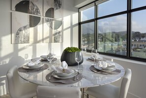 Un coin repas avec une table ronde dressée pour quatre personnes, une plante en pot et une vue sur la ville à travers de grandes fenêtres.