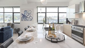 Una cocina moderna con ventanas amplias, un comedor con una mesa larga dispuesta para seis personas, y vista a la ciudad.
