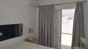 Ett hotellrum med en säng, ett nattduksbord, en lampa, en stol och en skjutdörr i glas som leder ut till en balkong.