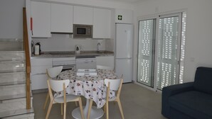 Ett modernt kök med vita skåp, en mikrovågsugn och ett kylskåp. I matplatsen finns ett matbord med stolar och i vardagsrummet finns en soffa.