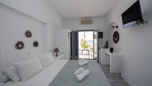 A hotel room with a bed, a TV mounted on the wall, and a balcony with a table and chairs. - Ostria Studios & Apartments (Paros)