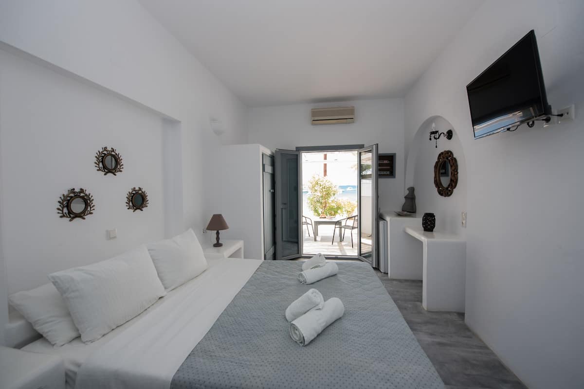 A hotel room with a bed, a TV mounted on the wall, and a balcony with a table and chairs.