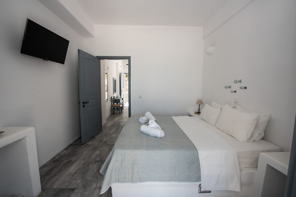 A hotel room with a bed, a TV mounted on the wall, and a door leading to a hallway.