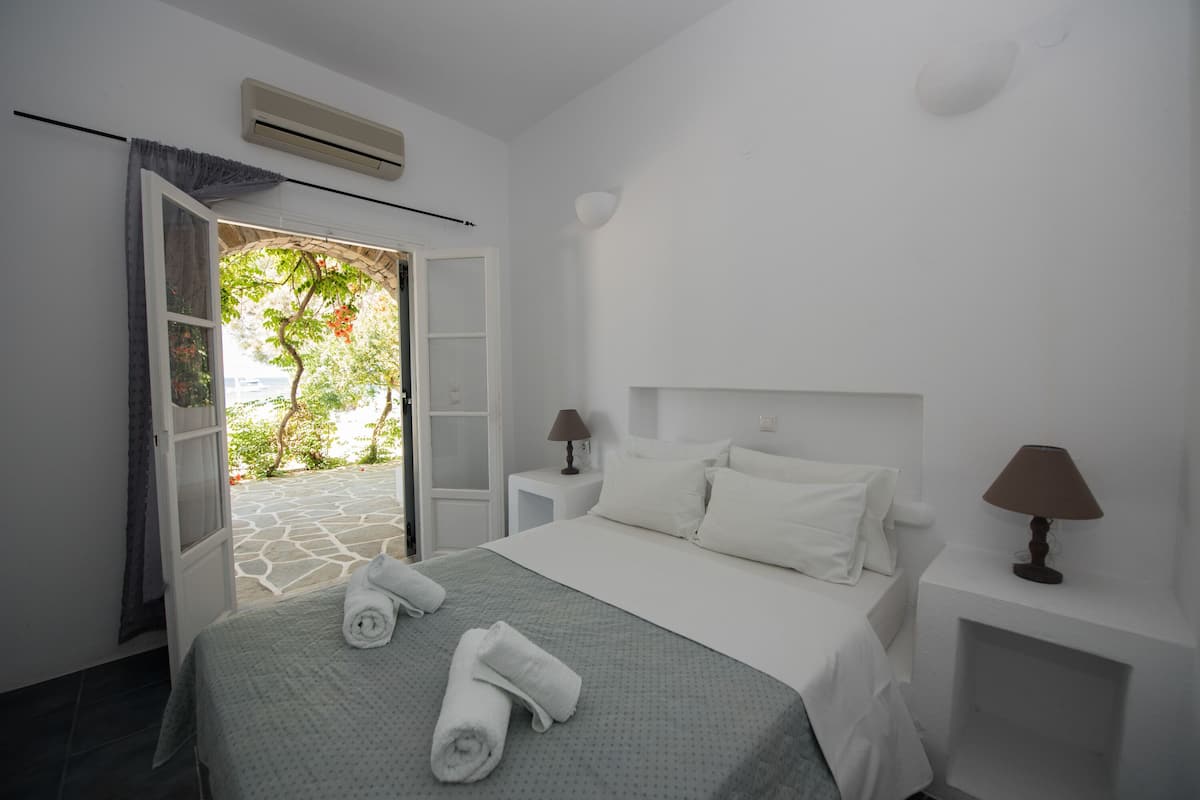 A hotel room with a bed, two bedside tables, a window with curtains, and an air conditioning unit.