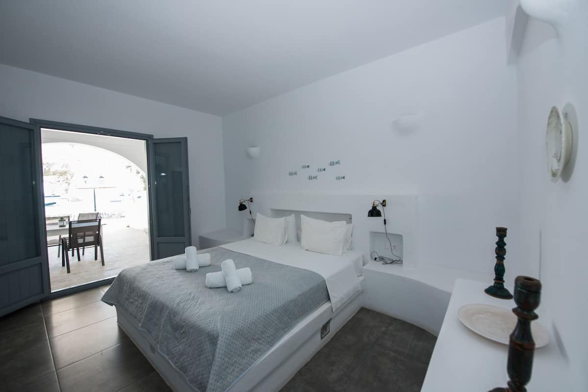 A modern bedroom with a bed, bedside tables, and a view through an open door to an outdoor area.