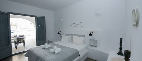 Quarto moderno com cama, mesas de cabeceira e vista para área externa através de uma porta aberta.