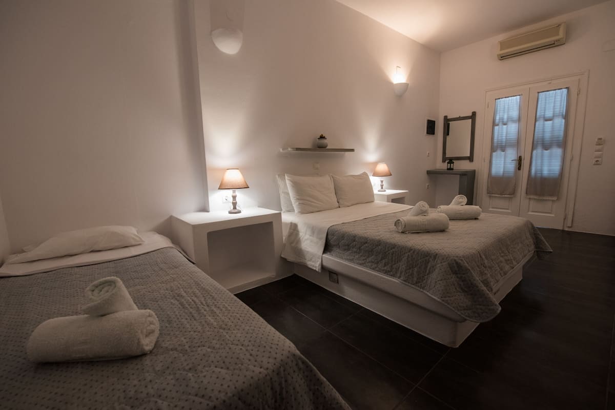 A hotel room with two beds, a bedside table with lamps, a shelf above the beds, and a mirror on the wall.