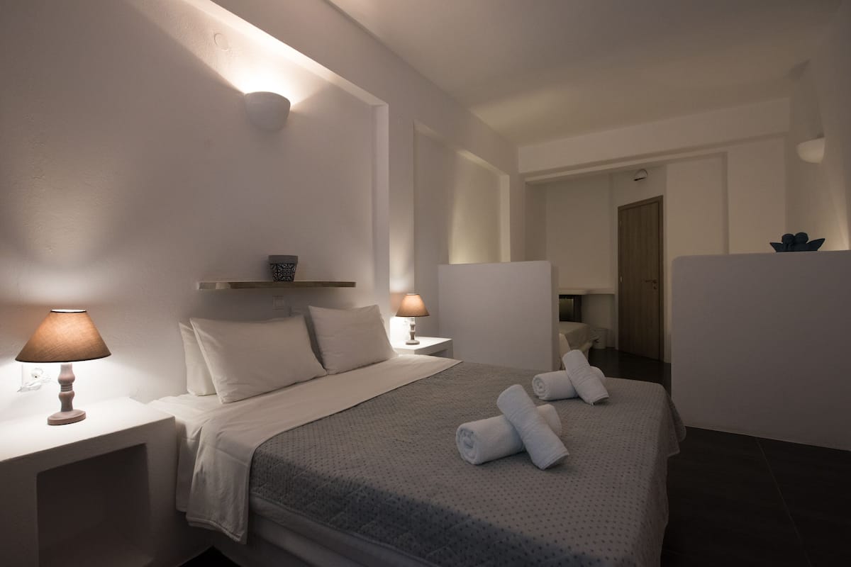A hotel room with a neatly made bed, two bedside lamps, and a door leading to a bathroom.