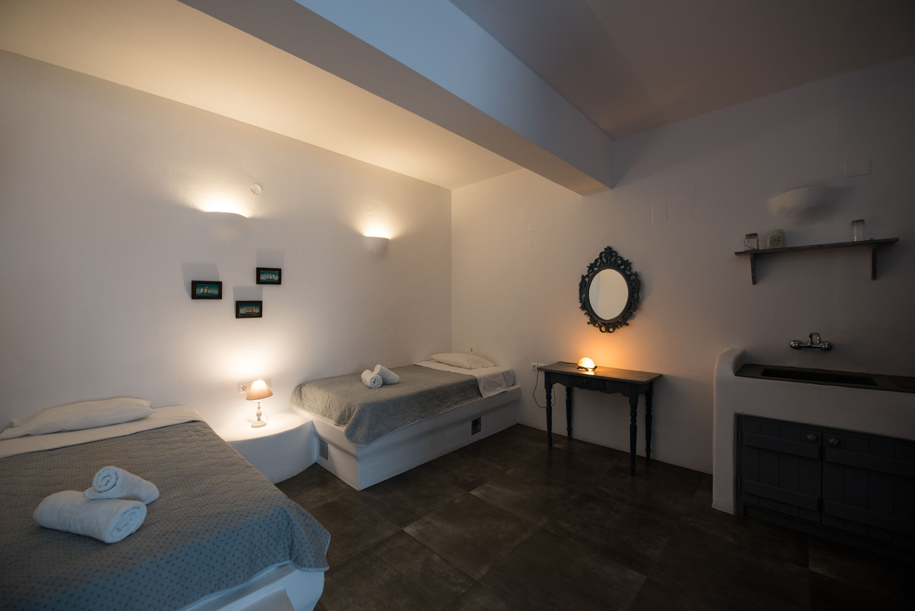 A bedroom with two beds, a bedside table with a lamp, a mirror, and a fireplace.