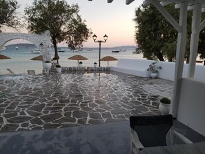 Un patio de piedra con sombrillas, una lámpara y vistas al mar con barcos.