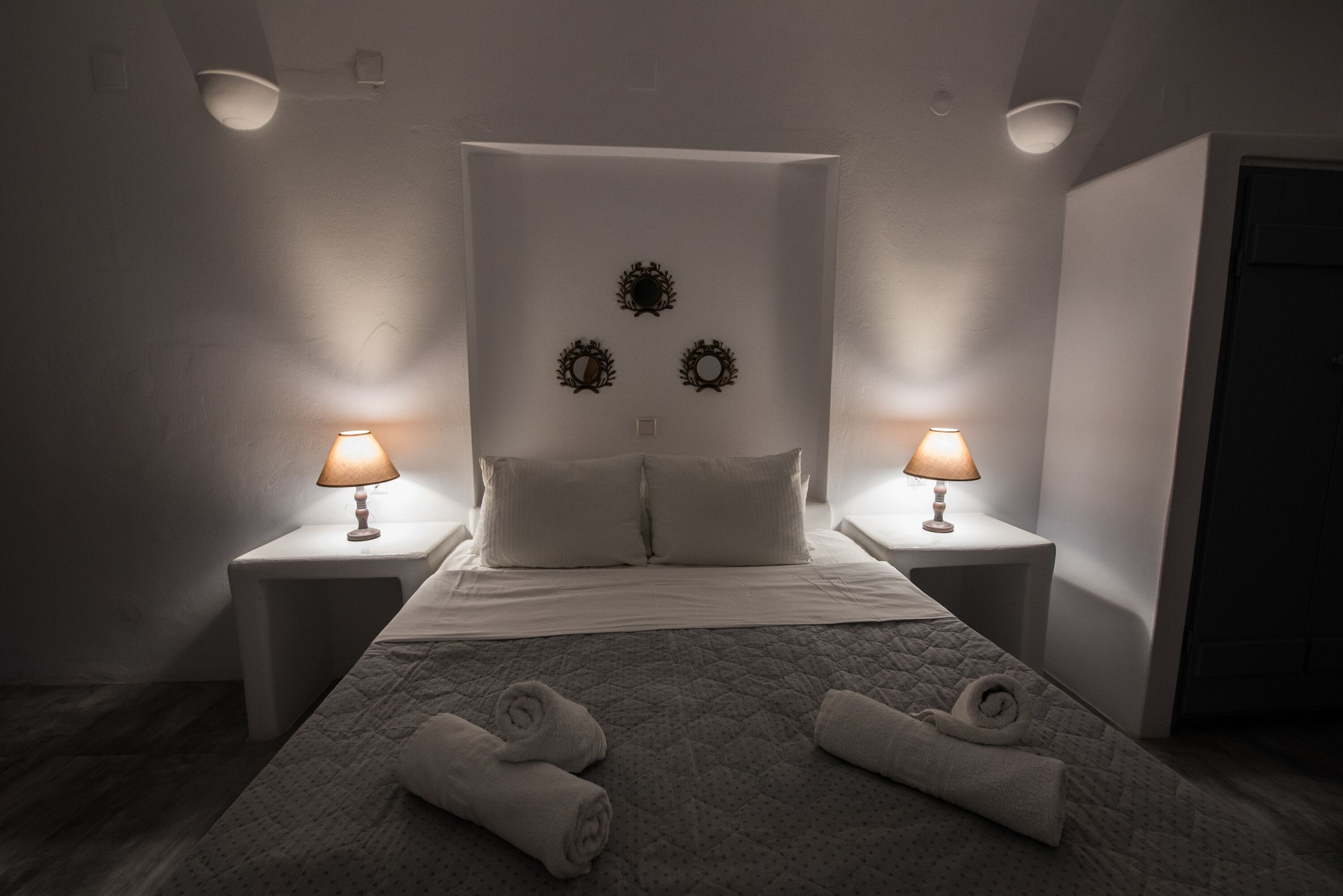 A hotel room with a bed, two nightstands with lamps, and a wall with three decorative wreaths.