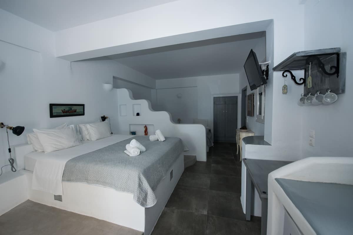 A modern hotel room with a bed, a desk, a TV, and a shelf with cups.