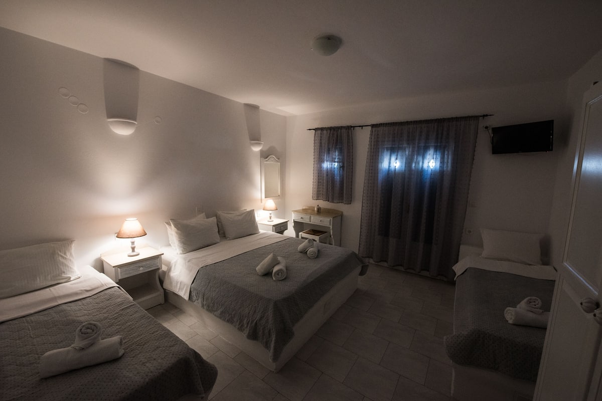 A hotel room with two beds, a nightstand with a lamp, a dresser, and a TV mounted on the wall.