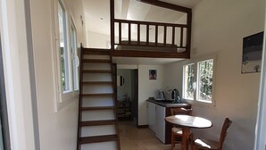 A compact, multi-level room with a wooden staircase, a dining area with a table and chairs, and a kitchen area. - Nuit Insolite en Tiny House (BEULOTTE SAINT LAURENT)