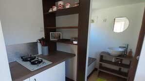 A compact kitchen with a gas stove, white cabinets, and a wooden shelf unit. - Nuit Insolite en Tiny House (BEULOTTE SAINT LAURENT)