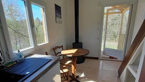 A compact kitchen with a sink, a wooden table, and chairs. There is a window providing natural light and a view of trees outside. - Nuit Insolite en Tiny House (BEULOTTE SAINT LAURENT)