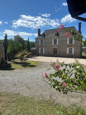 A stone building with a gravel driveway and a garden with pink flowers.