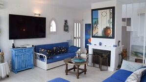 A living room with a blue sofa, a flat-screen TV, a fireplace, and a painting on the wall. - Villa with private pool very close to the beach.Capacity 8 people. Wifi. (pals)