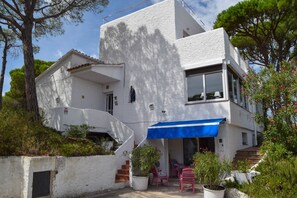 A white building with a blue awning, a staircase, and potted plants.