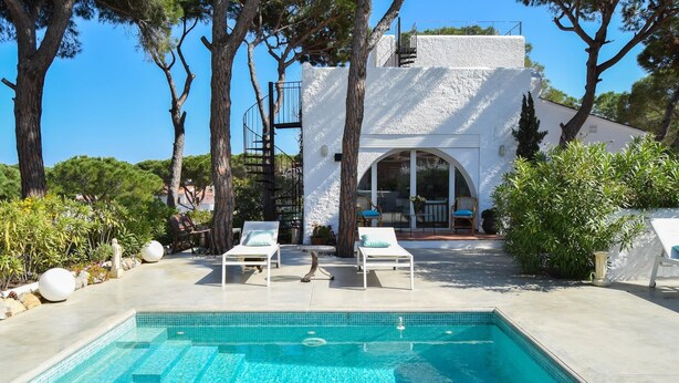A swimming pool with two lounge chairs, surrounded by trees and a white building with a covered patio. - Villa with private pool very close to the beach.Capacity 8 people. Wifi. (pals)