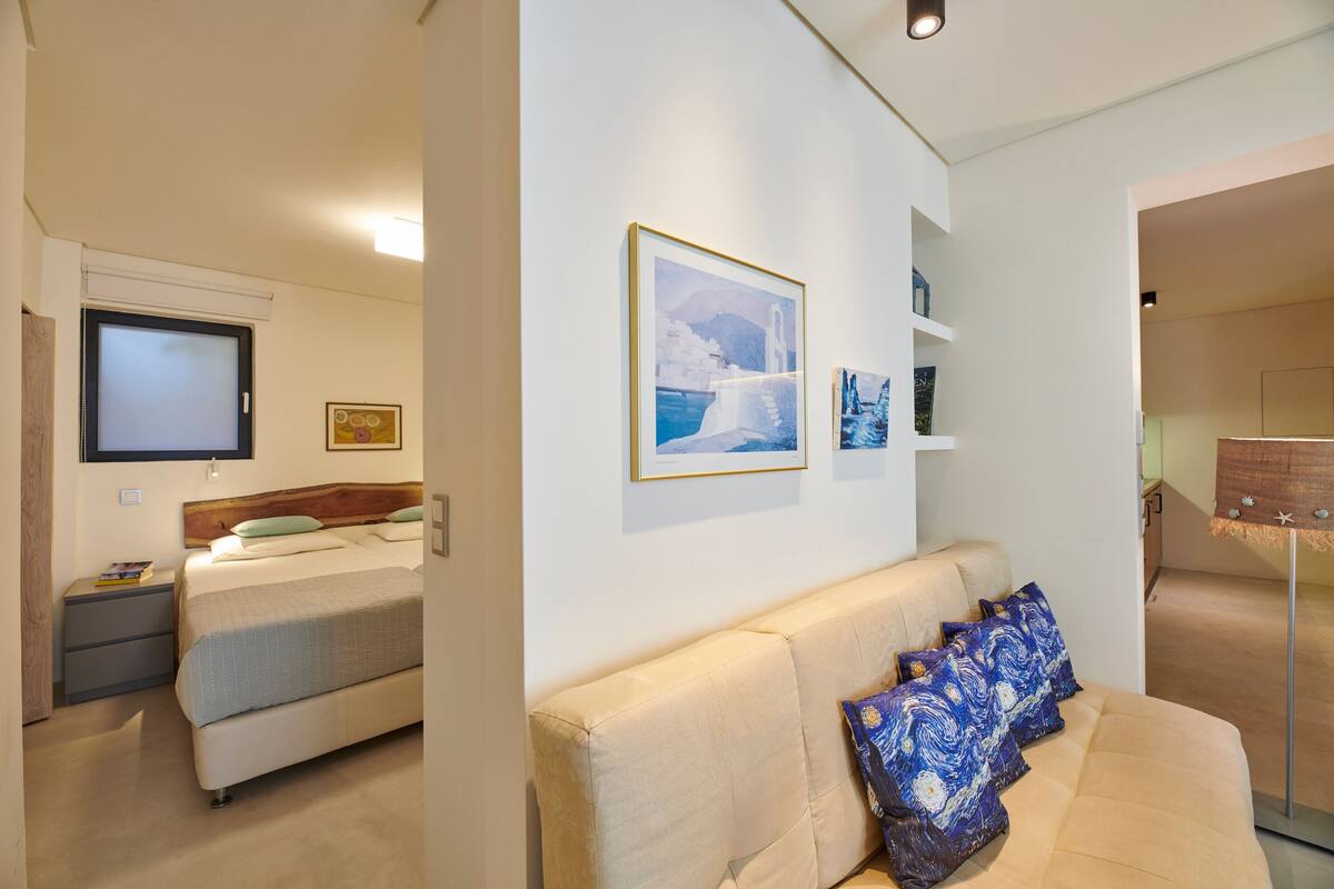 A hotel room with a bed, a sofa, a TV, and artwork on the walls.