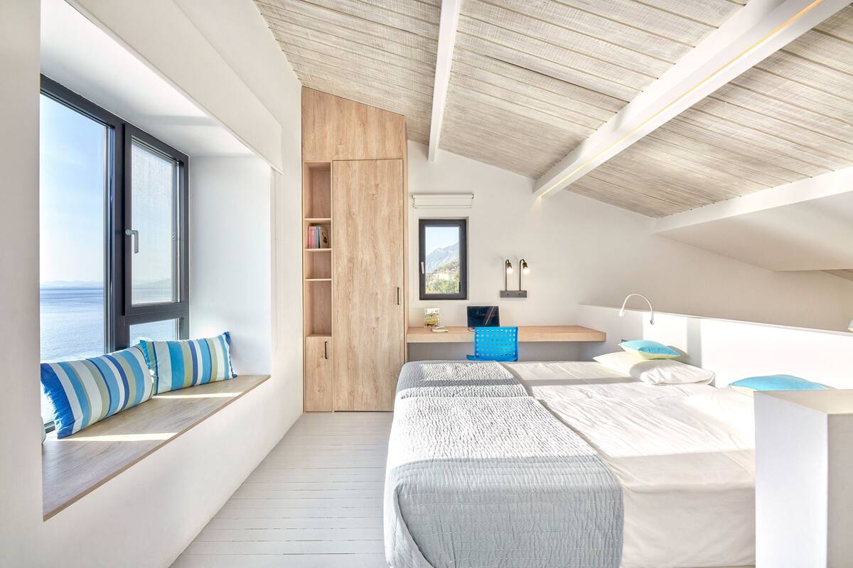 A modern bedroom with a large window, built-in bench, and a wooden wardrobe.