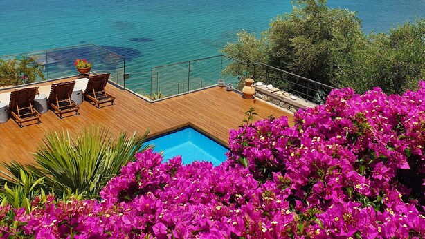 Ein Poolbereich mit Meerblick, einer Holzterrasse und leuchtenden Blumen.