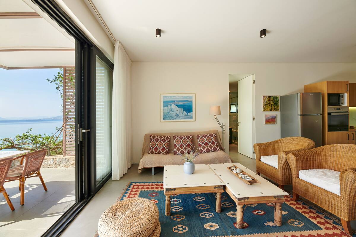 A modern living room with a sofa, two wicker chairs, a coffee table, and a view of the sea.