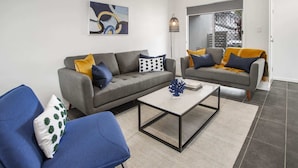 Ein modernes Wohnzimmer mit zwei grauen Sofas, einem Couchtisch und blauen Stühlen.