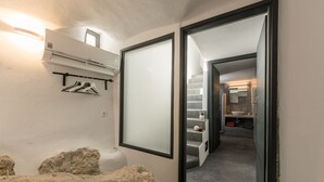 Een gang met een stenen muur, een kapstok en een badkamer zichtbaar door een geopende deur.