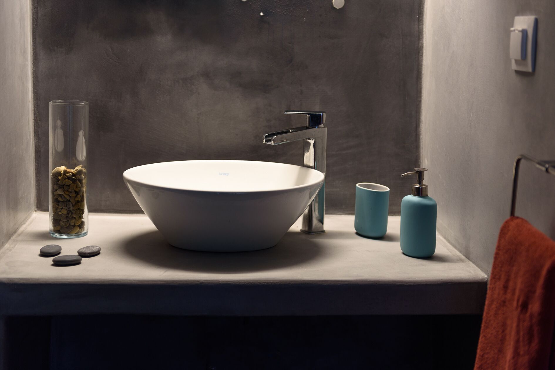 Een badkamer met een groot wit wastafel, een moderne kraan, een glazen pot met kiezelstenen en twee blauwe zeepdispensers.