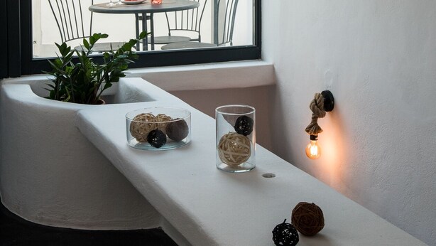Een moderne kamer met een witte bank, een plant in pot, decoratieve glazen bollen en een wandlamp.